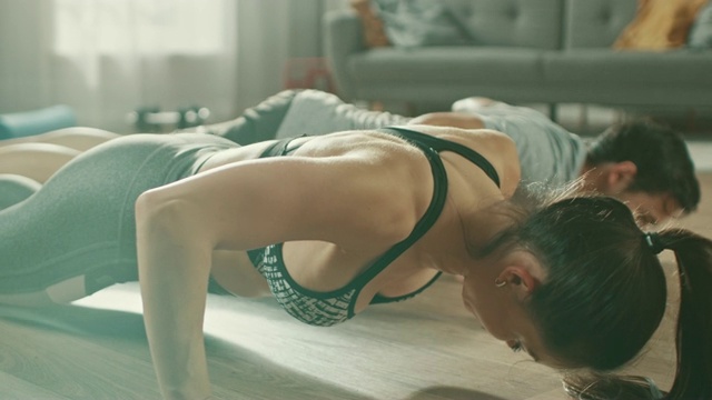 强壮美丽的运动健身夫妇穿着运动服在明亮宽敞的客厅里做俯卧撑运动。视频素材