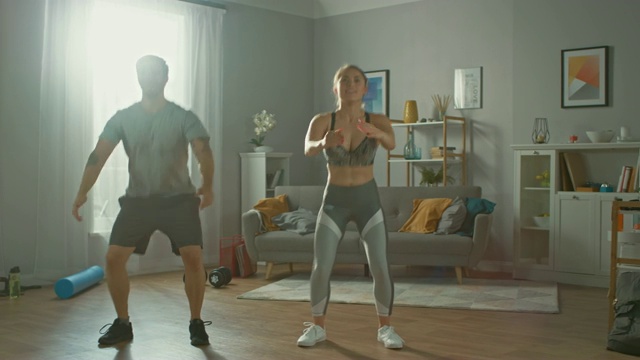肌肉男和美丽的健身女穿着运动服在他们明亮和宽敞的公寓里做下蹲练习。视频素材