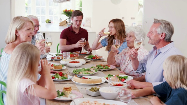 几代人围坐在家里的桌子上，在一起享用晚餐前敬酒-用慢镜头拍摄视频素材
