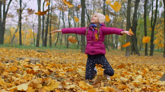 兴奋的女孩把秋天的落叶扔在公园里视频素材