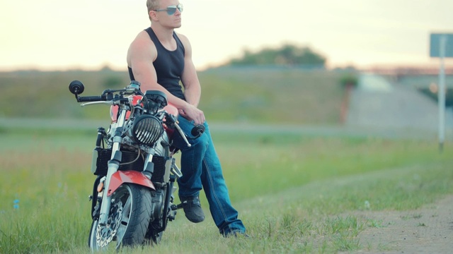一个戴着墨镜的骑摩托车的人坐在高速公路附近。摄像机从上到下拍摄视频下载