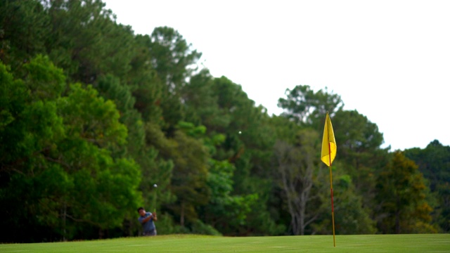 美丽的高尔夫球场，高尔夫球手在此球场打高尔夫球。果岭上有黄色旗子，球员向洞击球时视线模糊。视频素材