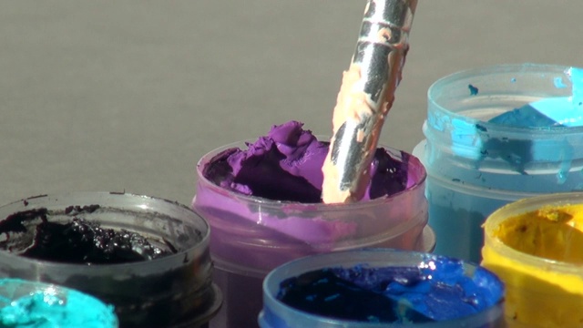 刷子浸入一罐紫色的丙烯酸水粉颜料中。家庭作业，艺术家的作品视频素材