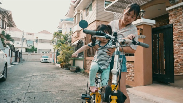 稳定的镜头:年轻的妈妈教她的女儿骑自行车视频素材