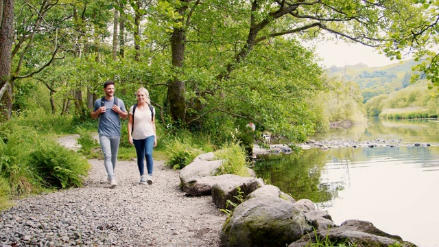在英国湖区，一对年轻夫妇沿着河边徒步旅行的慢镜头视频下载