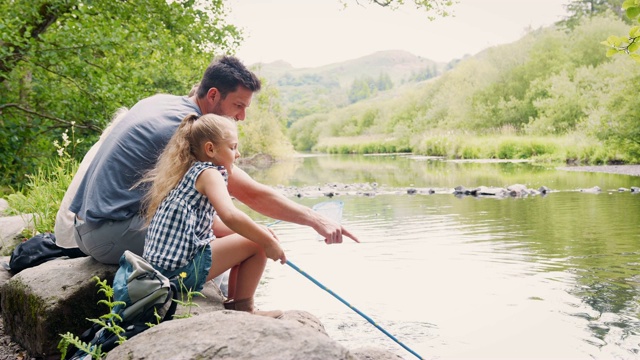英国湖区，一家人坐在石头上用渔网捕鱼的慢镜头视频下载