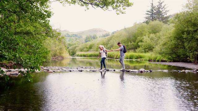 在英国湖区徒步旅行的年轻夫妇用踏脚石过河的慢动作镜头视频下载