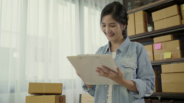 美丽聪明的亚洲年轻企业家女企业家企业主中小企业检查产品在股票和写在剪贴板在家里工作。小企业主在家办公的概念。视频素材