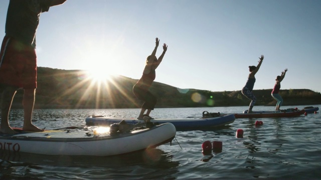 一群女性在椅子姿势(Utkatasana)瑜伽姿势，在一个晴朗，蓝色，阳光明媚的天空下，在西部科罗拉多沙漠湖的桨板上(斯努克斯波顿)视频下载