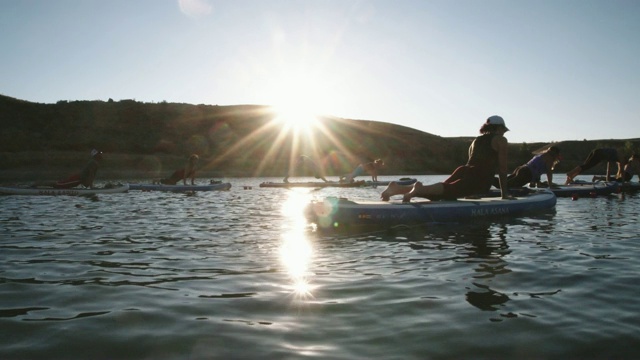 在科罗拉多西部晴朗、蓝色、阳光明媚的天空下，一群妇女在冲浪板上做下犬式瑜伽(斯努克斯图)视频下载