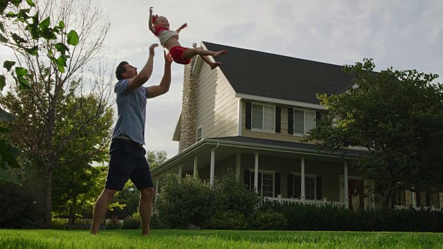 慢动作的父亲摆动和举起女儿在室外附近的房子/ Pleasant Grove，美国犹他州视频素材