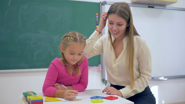 个人教育，有经验的导师教聪明的女孩在桌子附近的黑板在学校的教室视频下载