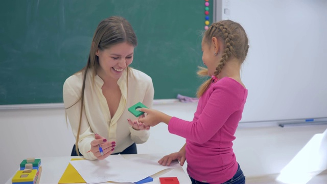 儿童教育，年轻的家教使用塑料数字教聪明的女学生在餐桌附近的学校的教室视频下载