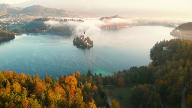 在雾蒙蒙的日出时分，与小岛上的小教堂环绕浪漫的流血湖飞行视频下载
