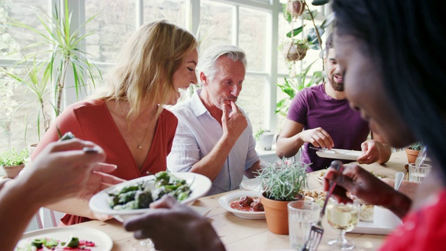 一个混合年龄的成年朋友群一起在一个小餐馆的桌子上吃饭，选择性的焦点视频素材
