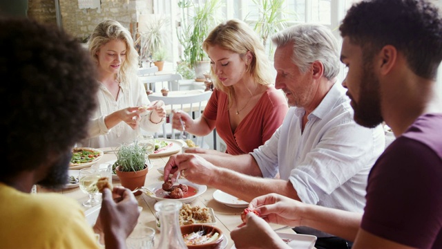 一个多民族，混合年龄的成年朋友群一起在餐馆的桌子上吃小吃，近距离，选择性的焦点视频素材