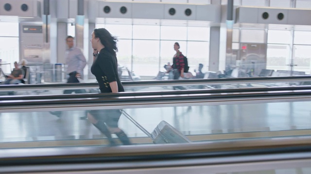 在机场候机楼的移动人行道上，电话中的女商人从两名旅客身旁匆匆走过。视频素材