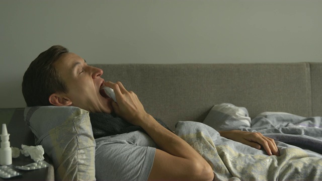 一名男子在家中卧病在床，旁边是他的药物，他在她的喉咙里洒了一种喉咙喷雾剂视频素材