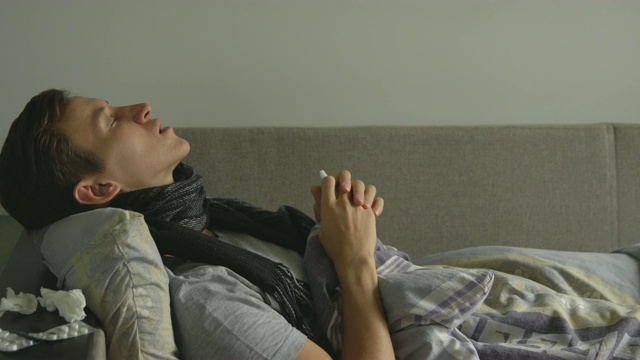 一名男子躺在病床上，旁边是他的药物，他往自己的鼻子里喷鼻喷雾剂视频素材