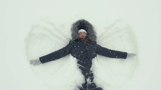 快乐的女孩躺在雪地上，像天使一样。视频下载