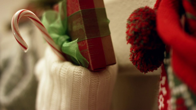 圣诞老人戴着手套的手把一个红白条纹拐杖糖放在圣诞长袜里，挂在壁炉架上视频下载