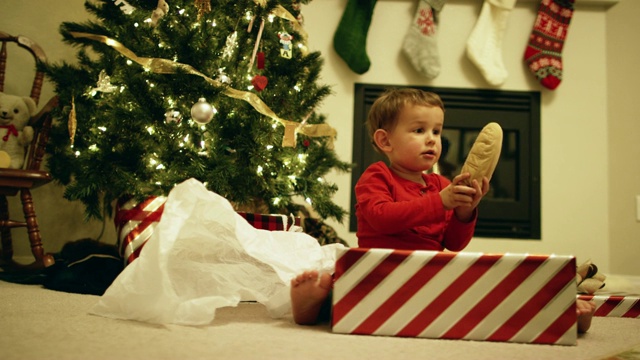 一个快乐、兴奋的三岁白人男孩在圣诞节那天在圣诞树旁打开一份圣诞礼物视频下载
