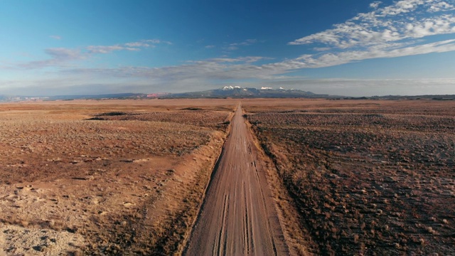 上升无人机拍摄的消失点土路与山脉的背景摩押外，犹他州与沙漠平原两侧的蓝天日落/日出视频下载