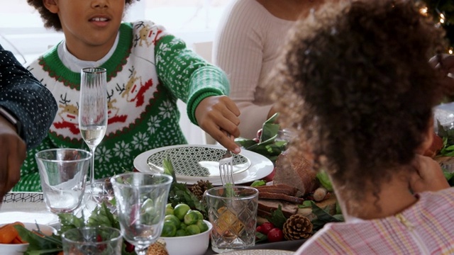 多代混血家庭围坐在圣诞餐桌前一起吃饭，用平底锅拍摄视频素材