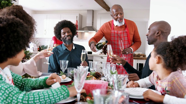 穿着围裙的黑人老人在餐桌上为家人倒香槟庆祝圣诞晚餐已经准备好了，选择性聚焦视频素材