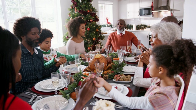 多代混血家庭坐在圣诞节餐桌上手牵着手，说恩典，选择性集中，高瞻远瞩视频素材