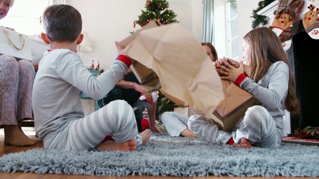 一家三代穿着睡衣在家里的休息室在圣诞节打开礼物视频素材