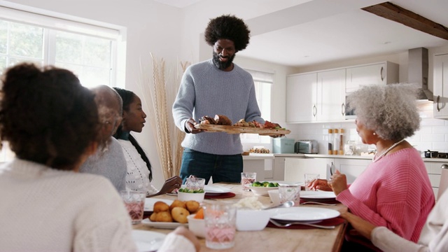 周日的家庭晚餐上，一对夫妇带着孩子和祖父母把食物端到餐桌上视频素材
