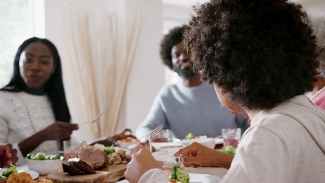 十几岁的黑人男孩坐在餐桌前和家人一起吃周日午餐，侧视，选择性关注视频素材