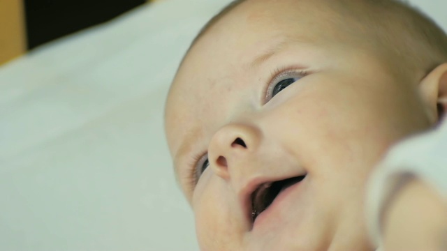 一个快乐的新生婴儿的特写，微笑着看着镜头，而他躺在床上的慢动作。视频素材