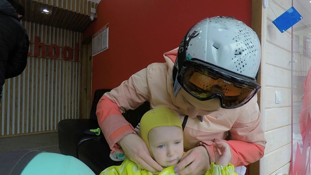 妈妈和滑雪教练给小女孩穿衣服。视频下载