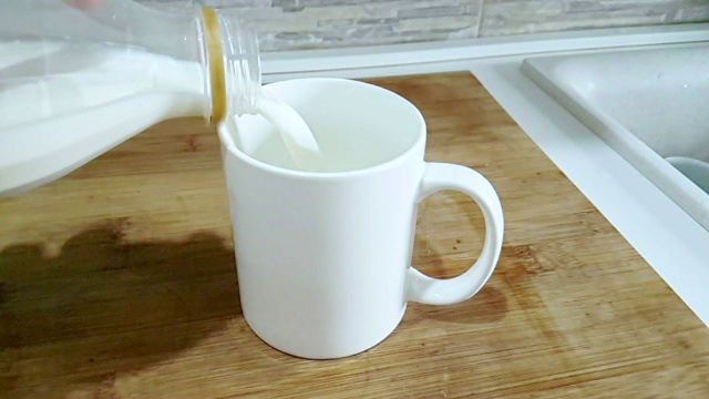 厨房背景上，鲜白牛奶倒进酒杯，慢镜头拍摄，饮食和健康营养早餐视频素材