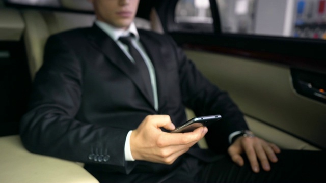 豪华汽车领域的成功商人，滚动智能手机，阅读电子邮件应用程序视频素材