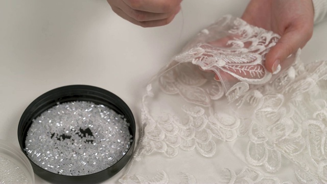 一个女人的手拿着有图案的织物，从她面前的盖子上缝下白色的珠子来装饰它视频下载