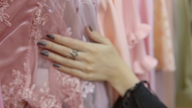 一个女人的手穿过一排衣服，在精品店里浏览。视频下载