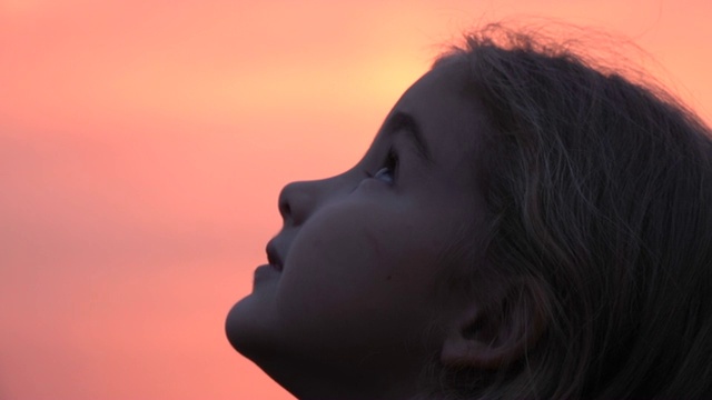 孩子在大自然中仰望天空。小女孩祈祷着仰望着紫色的天空，带着希望，特写。视频下载