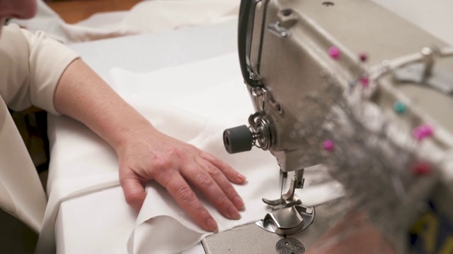 一个女人的手在缝纫机上缝合白色织物的特写俯视图。缝制婚纱的过程视频素材