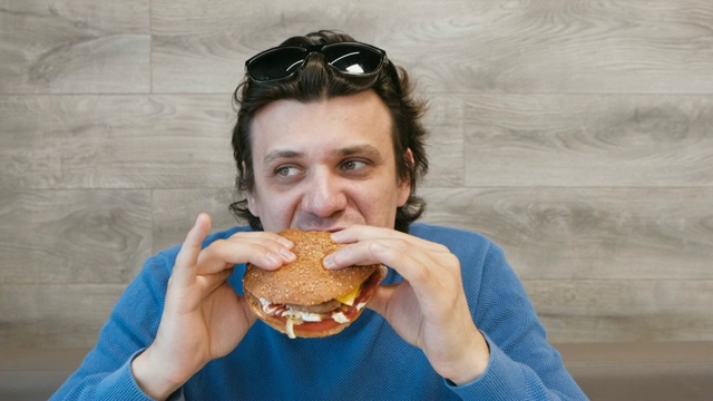 一个年轻人坐在咖啡馆里吃汉堡包。视频素材