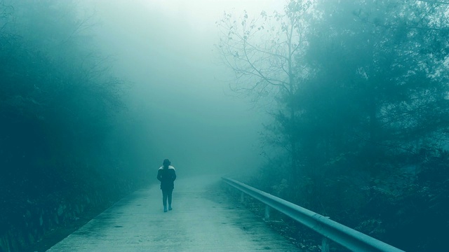 一个年轻女子孤独地走在雾蒙蒙的路上视频素材