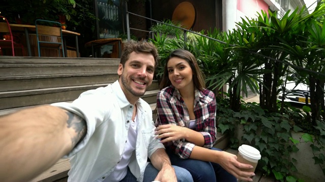 一对幸福的情侣坐在咖啡店外的楼梯上，对着相机自拍视频素材