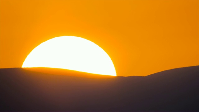巨大的太阳在地平线上缓缓升起，在水平的山脊后面露出了温暖的橙色色调。视频素材