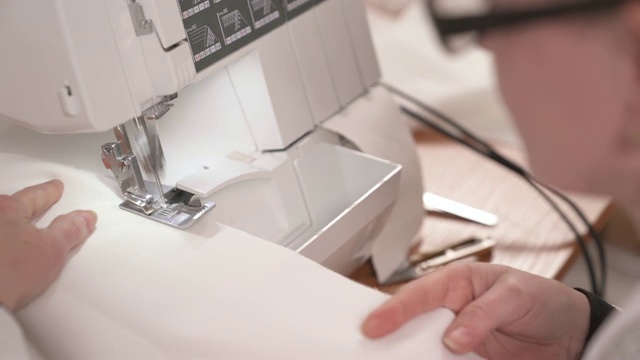 一位女裁缝在缝纫机上缝制白色织物的特写俯视图。缝制婚纱的过程视频素材
