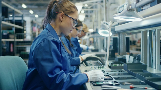 身穿蓝色工作服、戴着防护眼镜的电子厂女工正在用镊子组装智能手机的印刷电路板。拥有更多员工的高科技工厂。视频素材