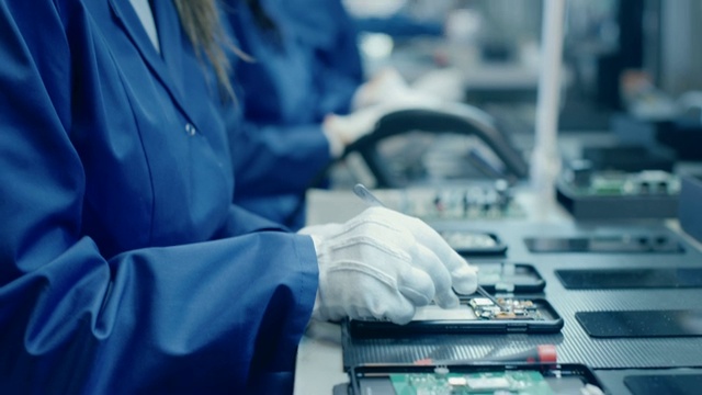 穿着蓝色工作服和防护眼镜的电子厂女工正在用镊子组装智能手机的印刷电路板。拥有更多员工的高科技工厂。视频素材