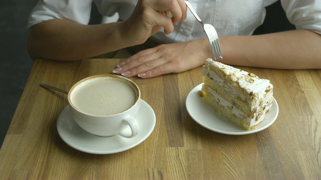 一个女孩在咖啡馆喝咖啡，吃一个甜蛋糕。女手的特写镜头视频素材