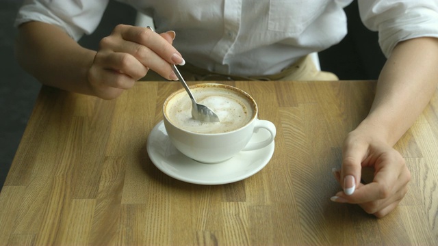 女孩的手搅拌着一杯拿铁咖啡中的糖视频素材